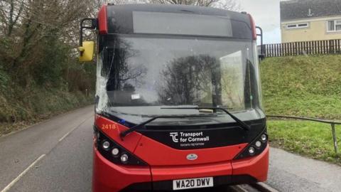 The front of a single decker red bus. The bus is parked. It says "Transport for Cornwall" on the front of the bus. 