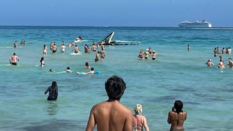 Beachgoers swim towards the crashed helicopter