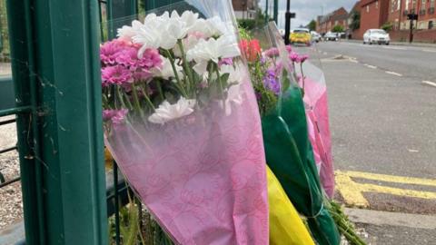 Flowers left at the scene as a tribute, with colours such as pink, yellow and green, placed next to a green railing