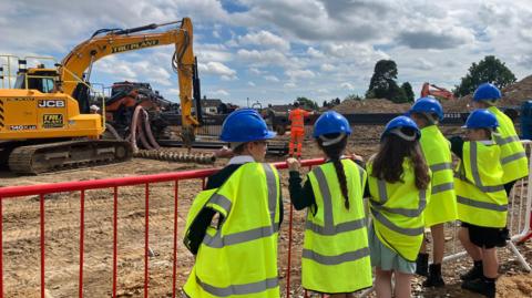 A group of six children standing in front of metal fences placed on the boundary of a construction site. 