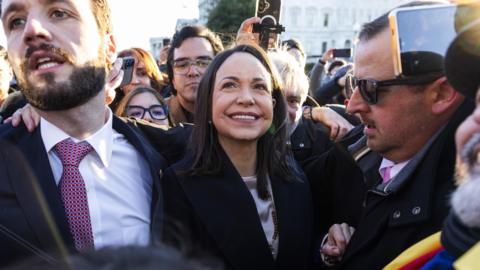 Maria Corina Machado smiles as she is guided by security through a crowd in Washington DC