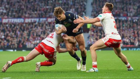 Wigan Warriors' Sam Walters is tackled by Hull KR's James Batchelor and Tom Davies during the Betfred Super League Grand Final match between Hull KR and Wigan Warriors at Old Trafford on October 11, 2025.