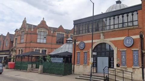 Bar 42 exterior, in Broadway, Peterborough. A red-brick and partially glass-fronted building with an outdoor space covered by black marquees. 