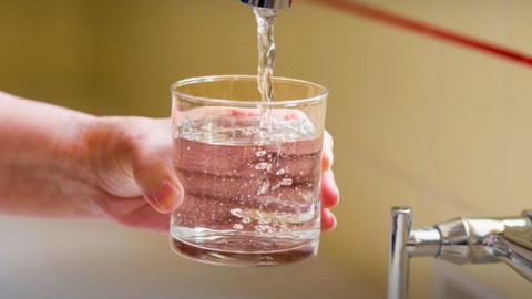 Someone pours a glass of tap water into a glass