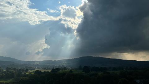 Crepuscular rays shining through a large cloud over rolling hills