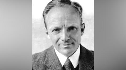 A black and white photo of a man with short hair and a grey suit