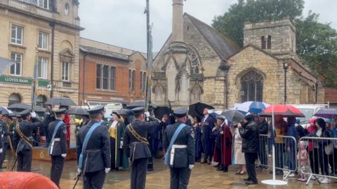 Military personnel gather in rainy weather saluting.