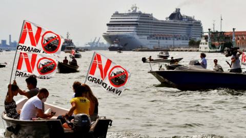 Protesters in boat in front of cruise ship, with signs saying 'no large ships'