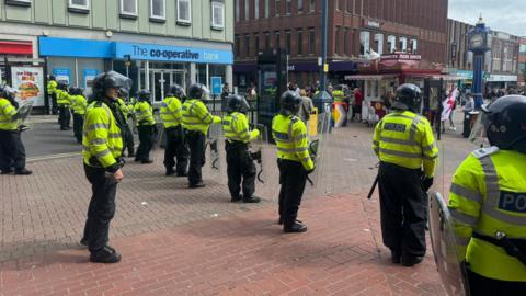 Police officers wearing police jackets and with riot gear lined up on a street in Hanley, Stoke-on-Trent.