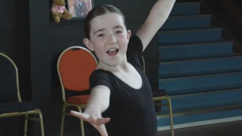 A young girl in a black leotard dancing