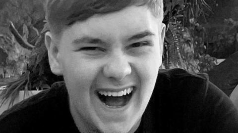 Black and white picture of a young man with his mouth open and laughing towards the camera. The boy is 15 year old Harvey Willgoose.