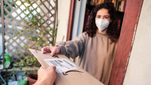 A woman wearing a mask accepts an Amazon package