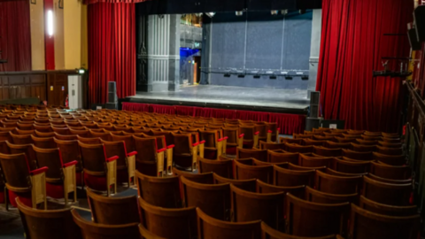 The main auditorium at The Albany Theatre with red and gold seats facing the stage with red curtains at each side