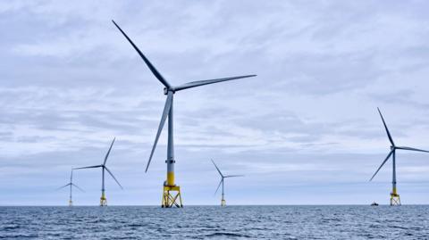 A set of offshore wind turbines out at sea with greyish blue skies in the background