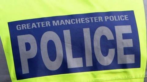 Close-up image of a police vest. Luminous yellow in colour with a blue box in the middle - within which 'Greater Manchester Police' is written in grey text.