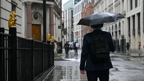 A man in a suit holds an umbrella in the street while it rains.