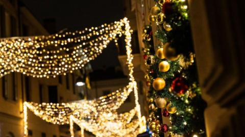 White Christmas street lights in the background with coloured lights and greenery in the right foreground