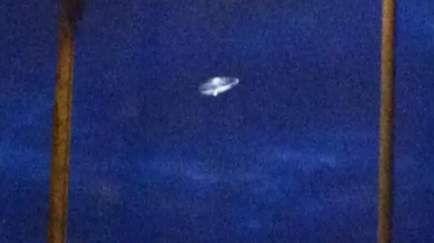 A grainy image shows a classic "flying saucer" set against a dark blue sky.