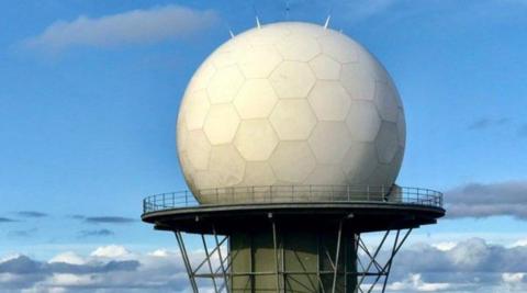 A dome, that looks like a golf ball, atop a platform and tower. Much of the image features blue sky or clouds.