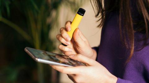 Young person holding vape whilst scrolling on phone