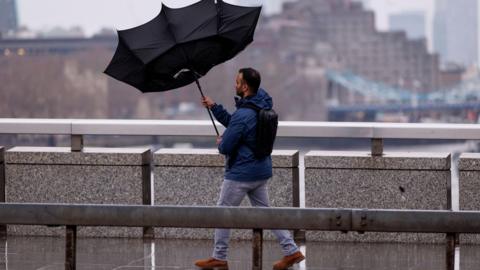 Man walks across bridge with inside out umbrella