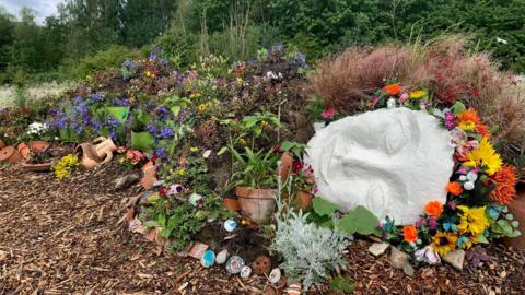 A reclining 'living sculpture', a female cast face with a floral headband and a body covered in flowers