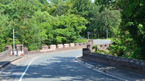 A road bridge in Dumfries and Galloway with sandstone barriers at the side and trees overhanging