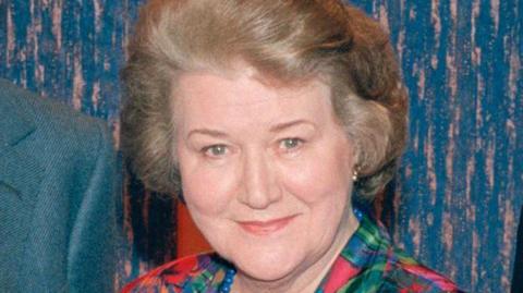 Dame Patricia Routledge, smiling at the camera, wearing a colourful blouse