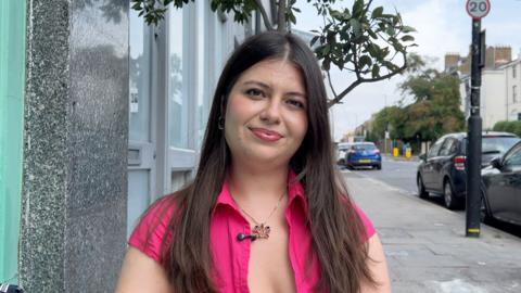 A girl with long brown hair and a pink shirt stands on a quiet street