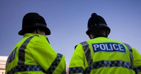 Two police officers are wearing hi-vis police jackets and helmets and are standing with their backs to the camera.