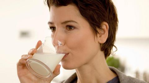 A woman with short brown hair drinks milk from a glass which is at her lips