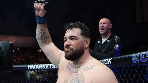 Louie Sutherland holds up his arm as he stands in the octagon