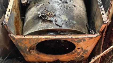 A burnt out tumble driver sitting in an alcove with charred walls