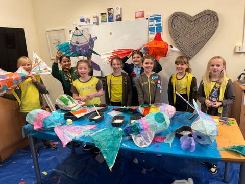 A group of 8 young girls in Brownies uniforms smile at the camera and hold up the colourful fish lanterns they have made for Gloucester's lantern parade