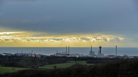 A general view of the skyline of the Sellafield site, pictured in between grassy fields and the sea.