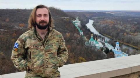 Jordan is pictured standing at a view point overlooking a valley. He is dressed in a camouflage uniform.