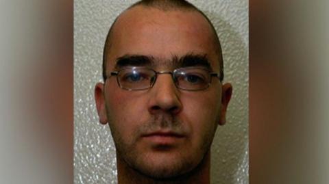 A man in his 20s, with close-cropped dark hair, thick eyebrows and metal-rimmed glasses, looking at the camera.