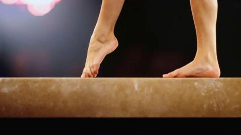 Only the feet of a gymnast can be seen as she poses on the beam 