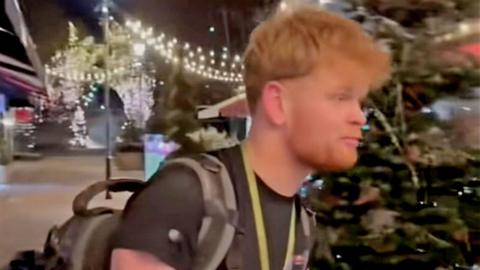 Young man with rucksack on looks at the camera and says 'I actually don't know how we are getting out'. 