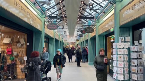 An indoor market, with green painted walls and stalls on either side