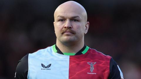 Tom Lawday, wearing the home Harlequins shirt with light blue, red and brown squares and black sleeves with green trim on the neck and sleeves.