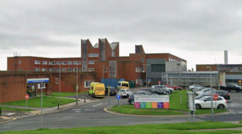 The exterior of Furness General Hospital. It is a red-brick building with cars parked at the front.