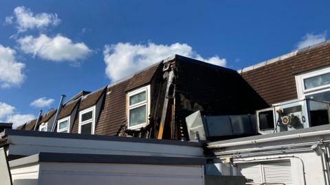 Image showing damage to part of a hotel roof, with white windows, against a blue sky and clouds. 