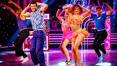 George Clarke & Alexis Warr on the Strictly Come Dancing stage, dancing a Salsa and wearing colourful outfits. Credit: BBC/Guy Levy