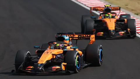 The McLaren of Lando Norris is pushed into position by his mechanics on the grid before the start of the Hugarian Grand Prix