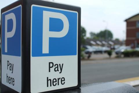 A close up of a parking metre on a street. Two sides of the cube are seen, with identical letter P against a blue background, and "Pay here" on a white background.