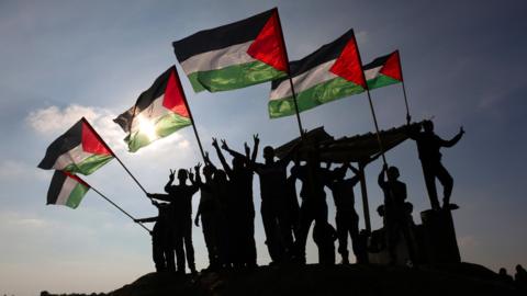 Palestinian protesters wave Palestinian flags near the Israel-Gaza border fence on 9 January 2018