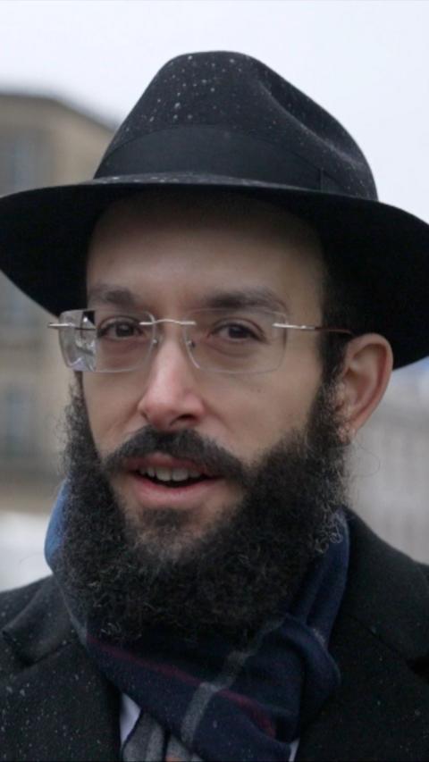 Bristol Rabbi wearing black hat and coat stood outside. He is smiling and is wearing glasses.