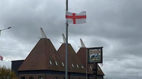 A St George's flag flaying on a lamp-post next to a sign which says Harrietsham.