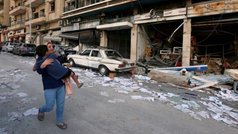 A woman carries a child as she walks past damaged shops following Tuesday"s blast in Beirut, Lebanon August 5, 2020